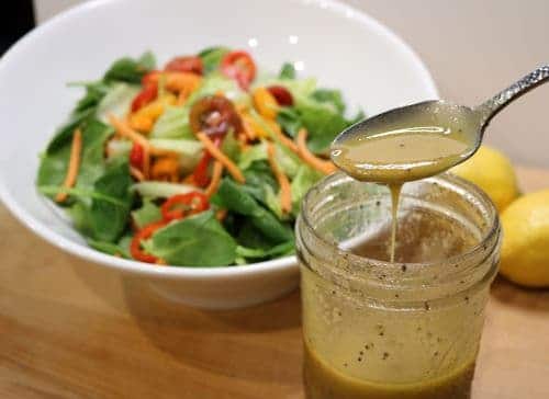 Vinaigrette dressing in front of a bowl of raw salad vegetables