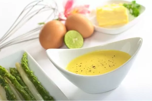 hollandaise sauce in a bowl with asparagus on platter
