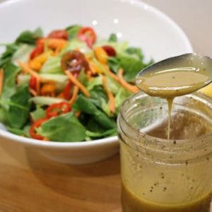 Vinaigrette dressing in front of a bowl of raw salad vegetables